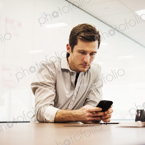 A young man sitting in a classroom at a table and looking down at a cellphone. A young man sitting in a classroom at a table and looking down at a cellphone.