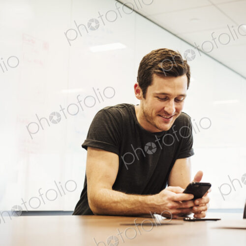 A young man sitting in a classroom at a table and looking down at a cellphone. A young man sitting in a classroom at a table and looking down at a cellphone.