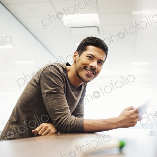 A young man sitting in a classroom leaning on a desk and smiling. A young man sitting in a classroom leaning on a desk and smiling.