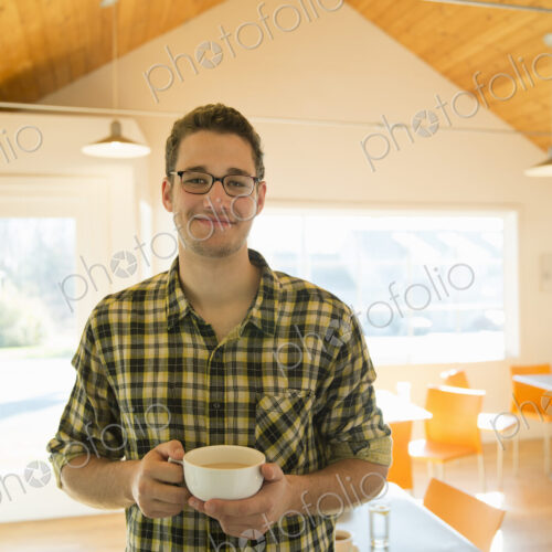 A young man standing holding a cup of coffee in a coffee shop. A young man standing holding a cup of coffee in a coffee shop.