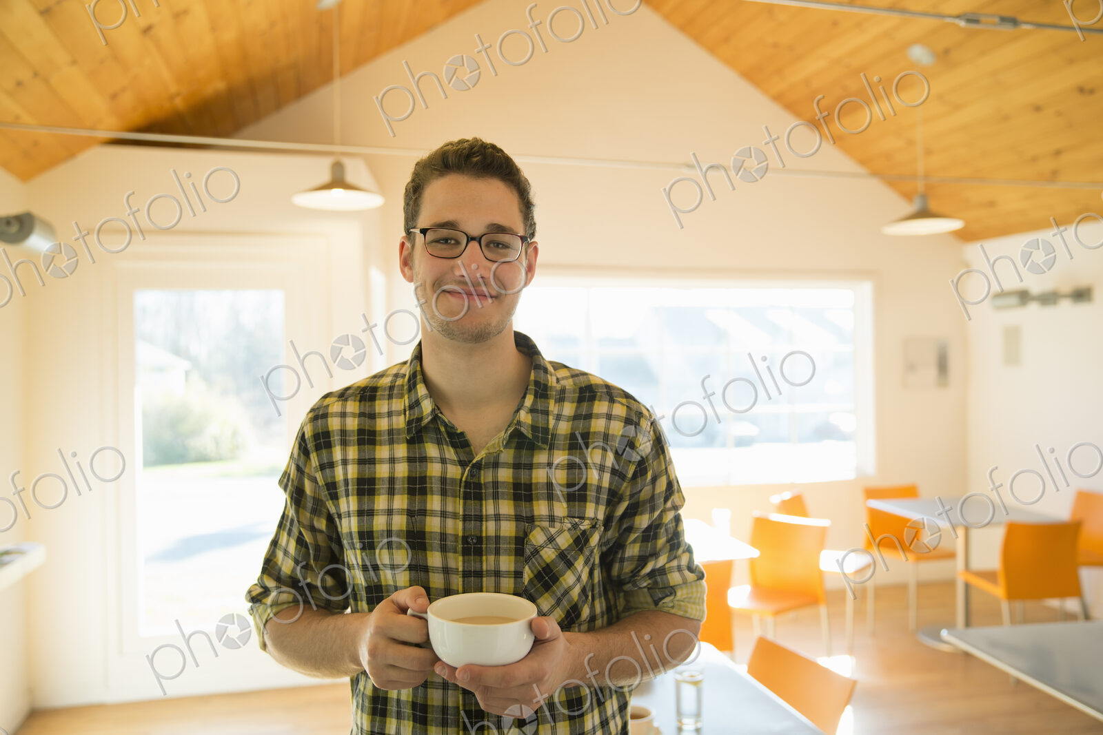A young man standing holding a cup of coffee in a coffee shop.