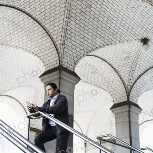 A young man standing on a stair under an archway, lookign at his mobile phone. A young man standing on a stair under an archway, lookign at his mobile phone.