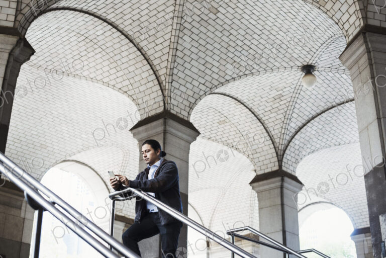 A young man standing on a stair under an archway, lookign at his mobile phone.