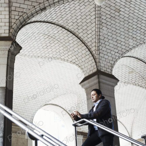 A young man standing on a stair under an archway, lookign at his mobile phone. A young man standing on a stair under an archway, lookign at his mobile phone.