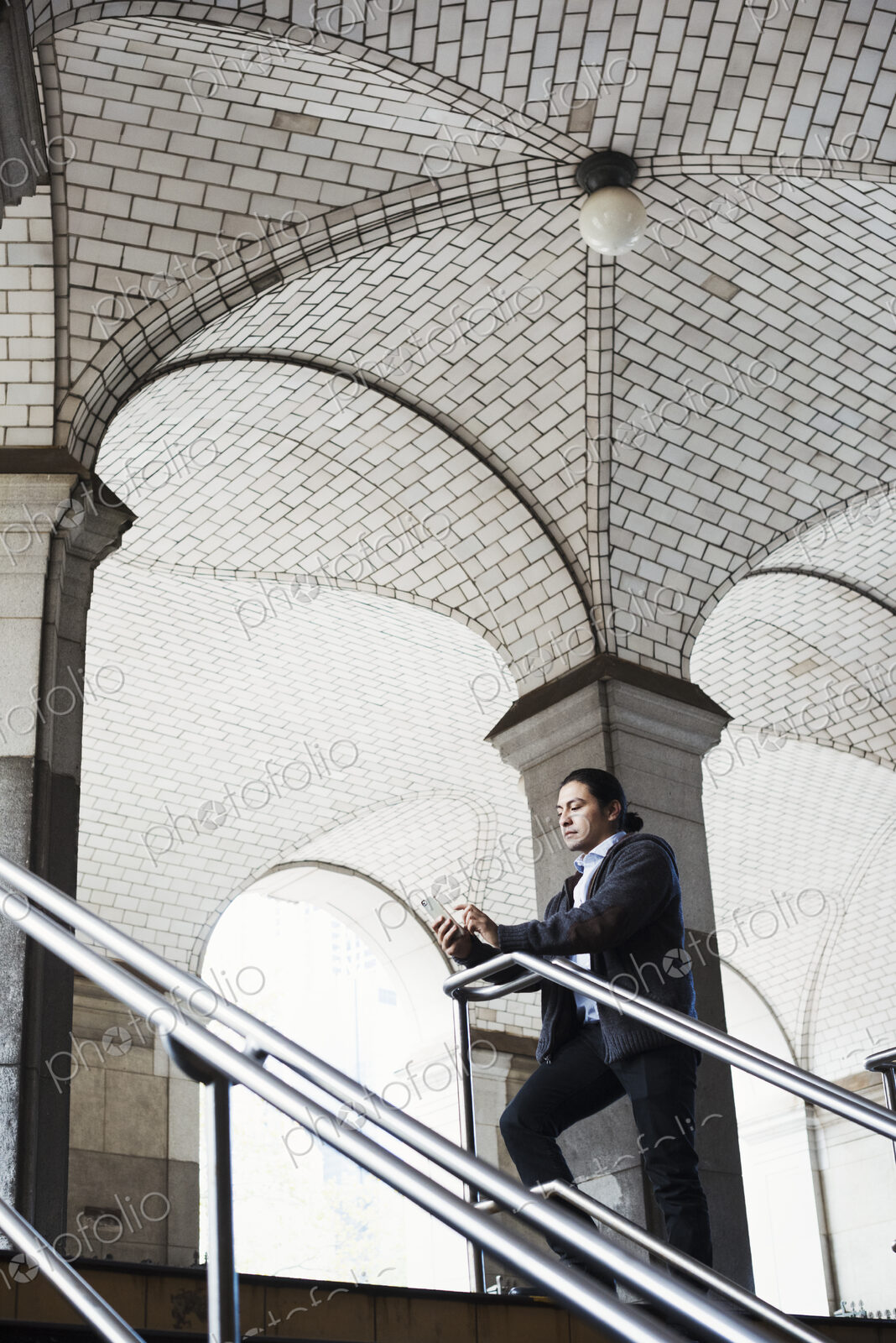 A young man standing on a stair under an archway, lookign at his mobile phone.