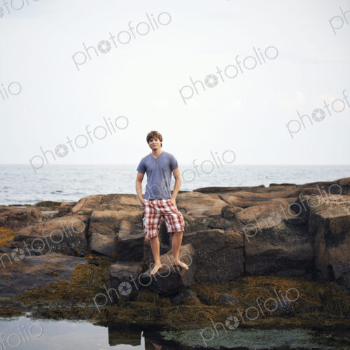 A young man standing on the shore by a rockpool with his hands in his pockets. A young man standing on the shore by a rockpool with his hands in his pockets.