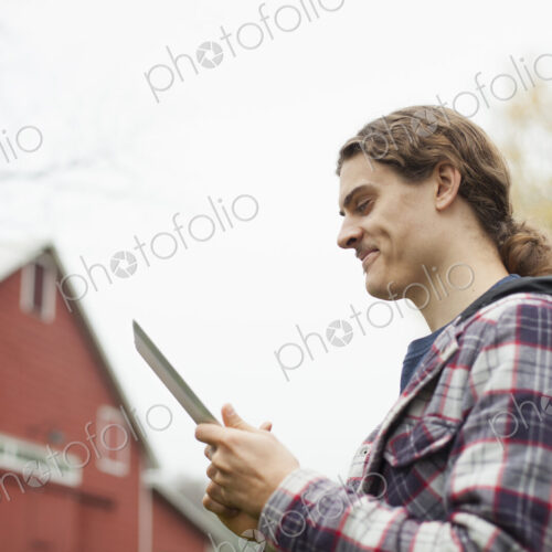A young man using a computer tablet, a portable PC tablet device, on an organic farm. A young man using a computer tablet, a portable PC tablet device, on an organic farm.