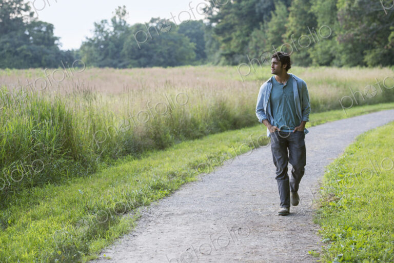 A young man walking down a path with his hands in his pockets.
