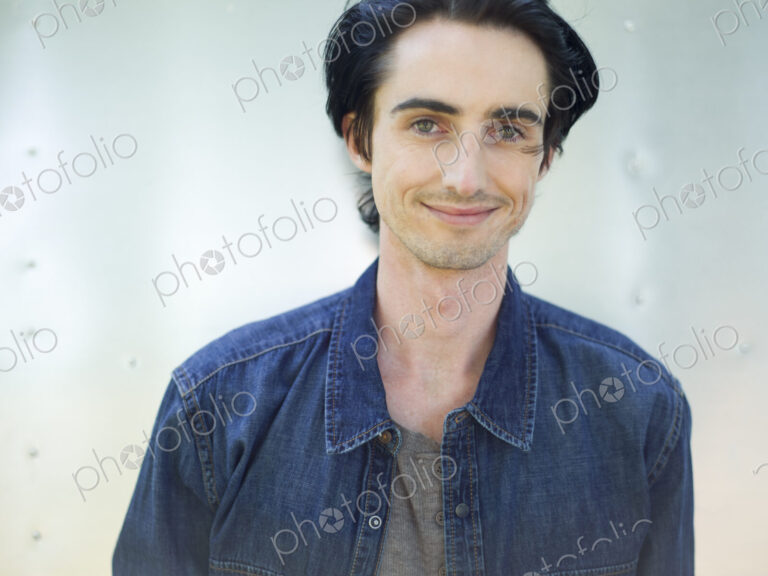 A young man wearing a denim shirt and hat.