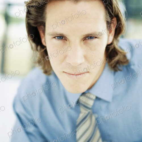 A young man with curly brown hair wearing a blue shirt and tie. A young man with curly brown hair wearing a blue shirt and tie.