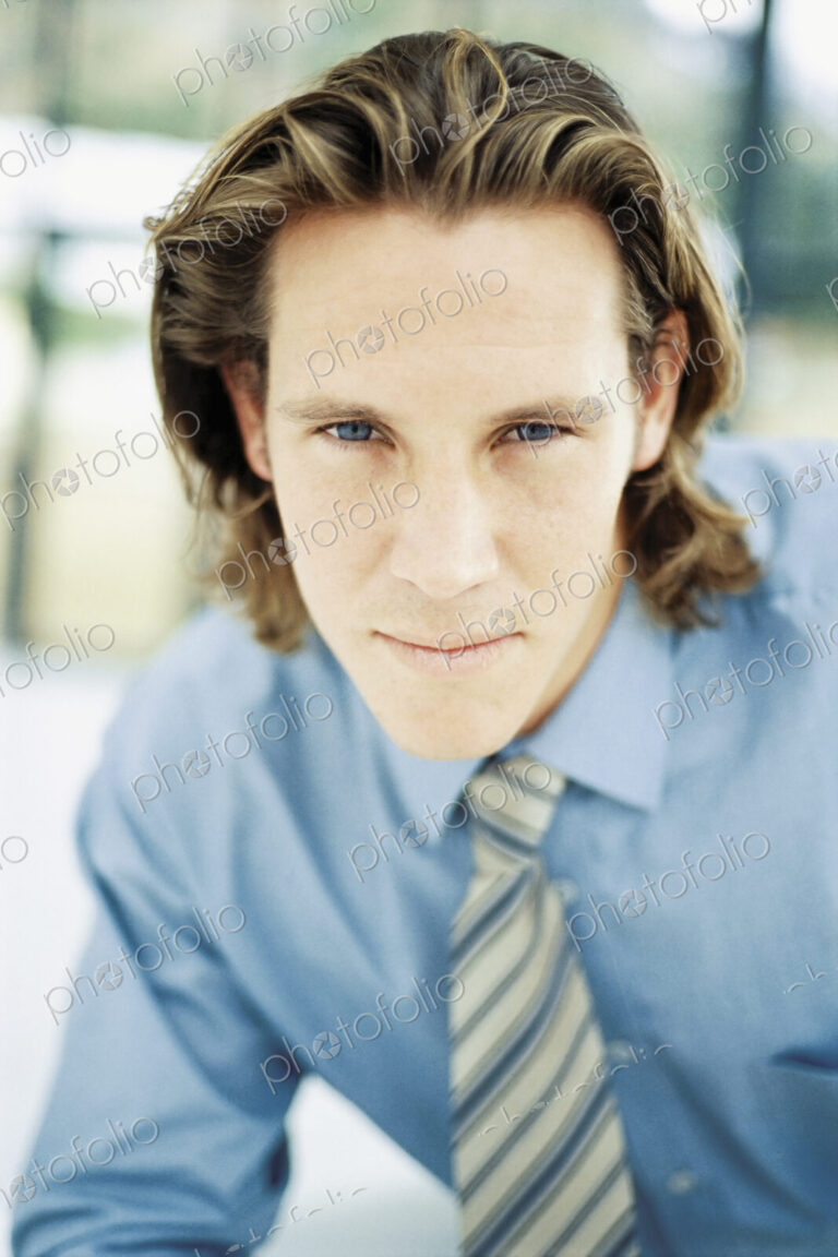 A young man with curly brown hair wearing a blue shirt and tie.