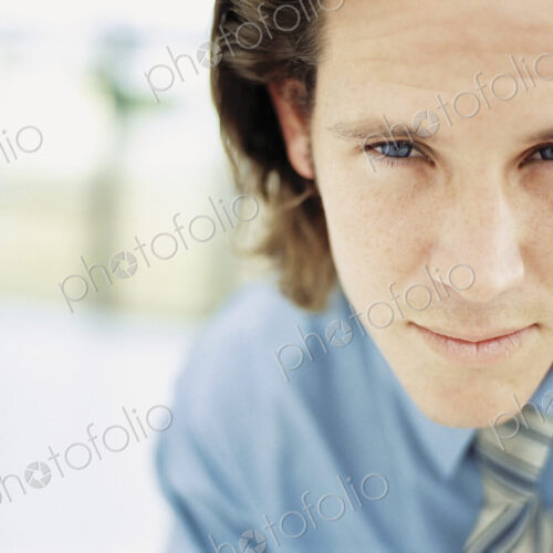 A young man with curly brown hair wearing a blue shirt and tie. A young man with curly brown hair wearing a blue shirt and tie.
