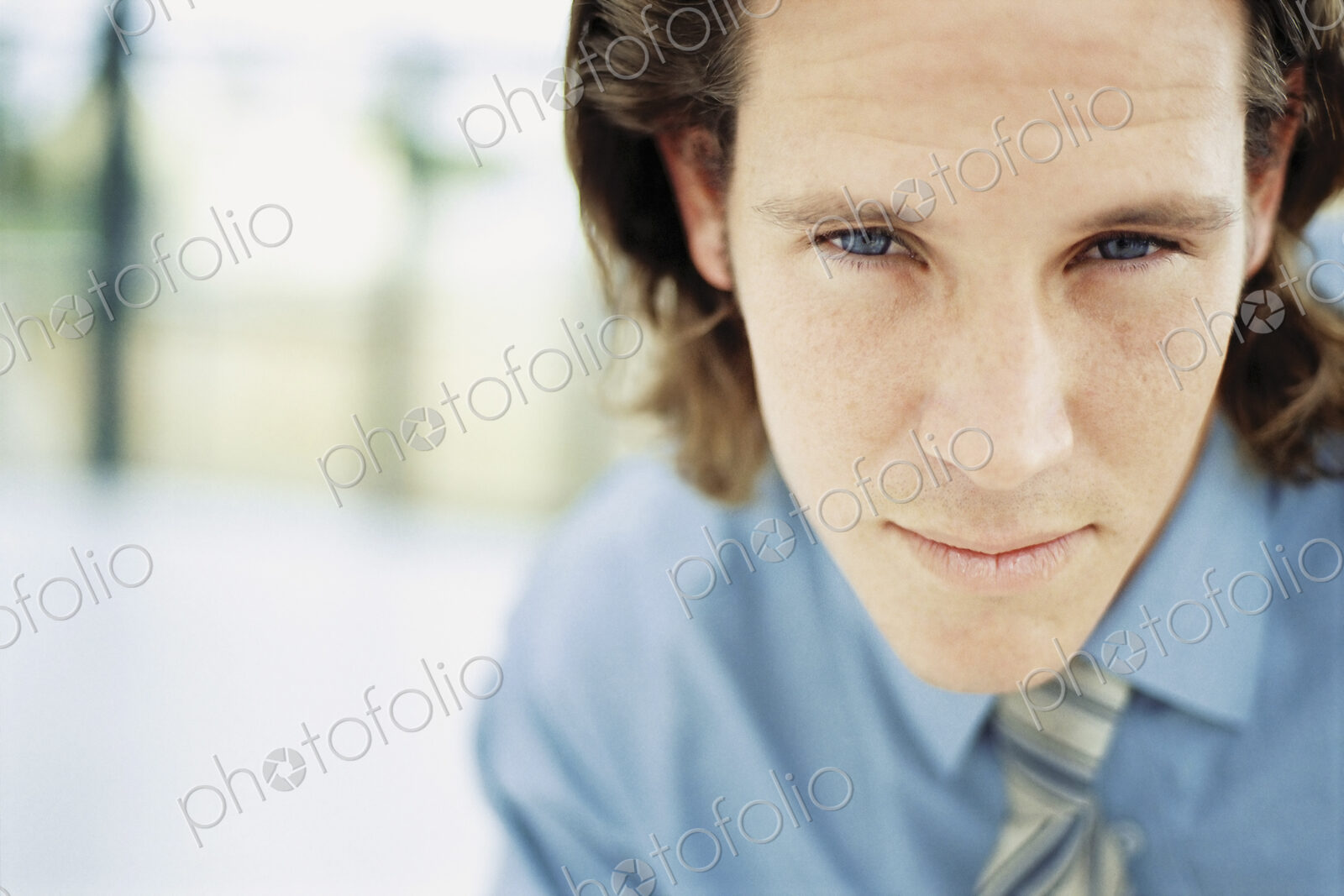 A young man with curly brown hair wearing a blue shirt and tie.