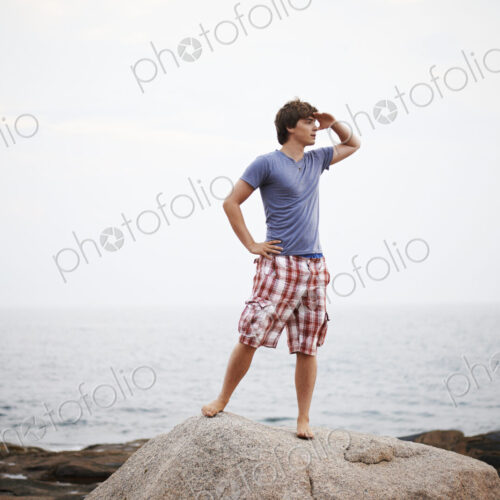 A young man with his hand to his head, shading his eyes and looking out from the… A young man with his hand to his head, shading his eyes and looking out from the…