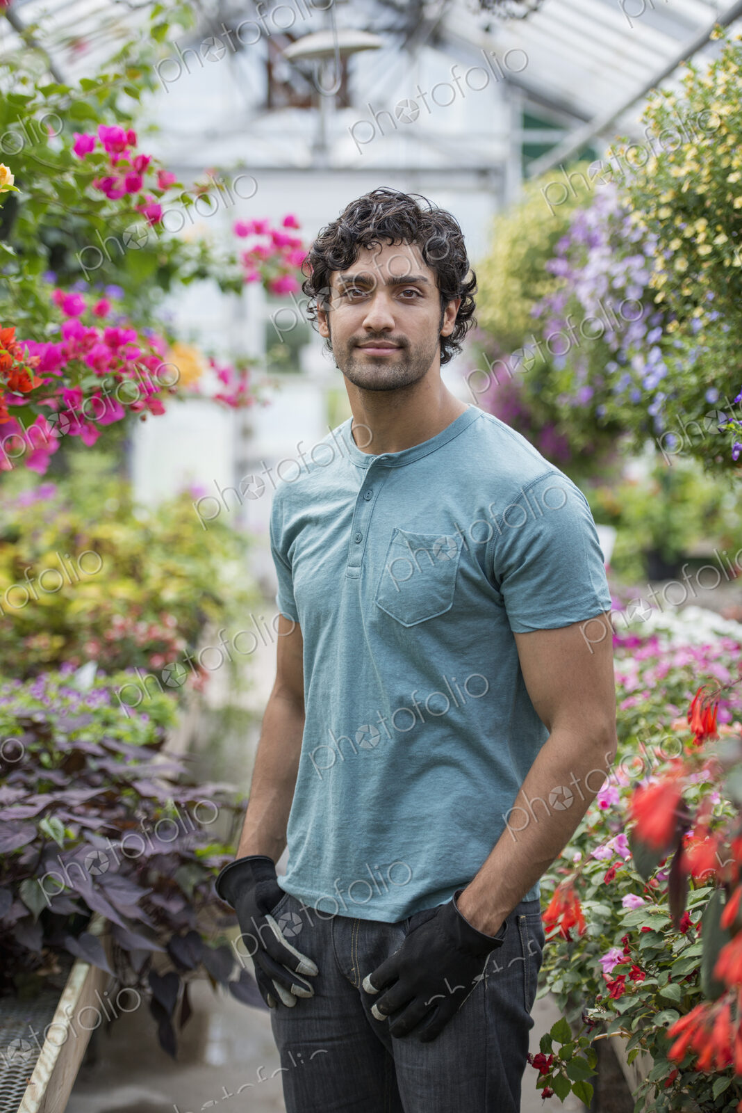 A young man working in a greenhouse full of flowering plants.