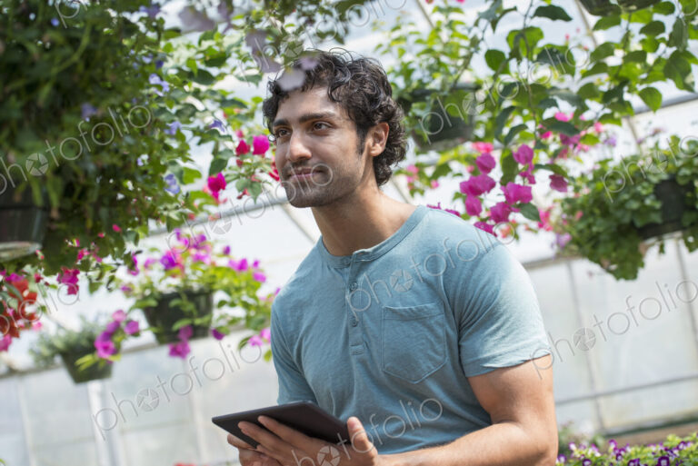 A young man working in a plant nursery, surrounded by flowering plants.