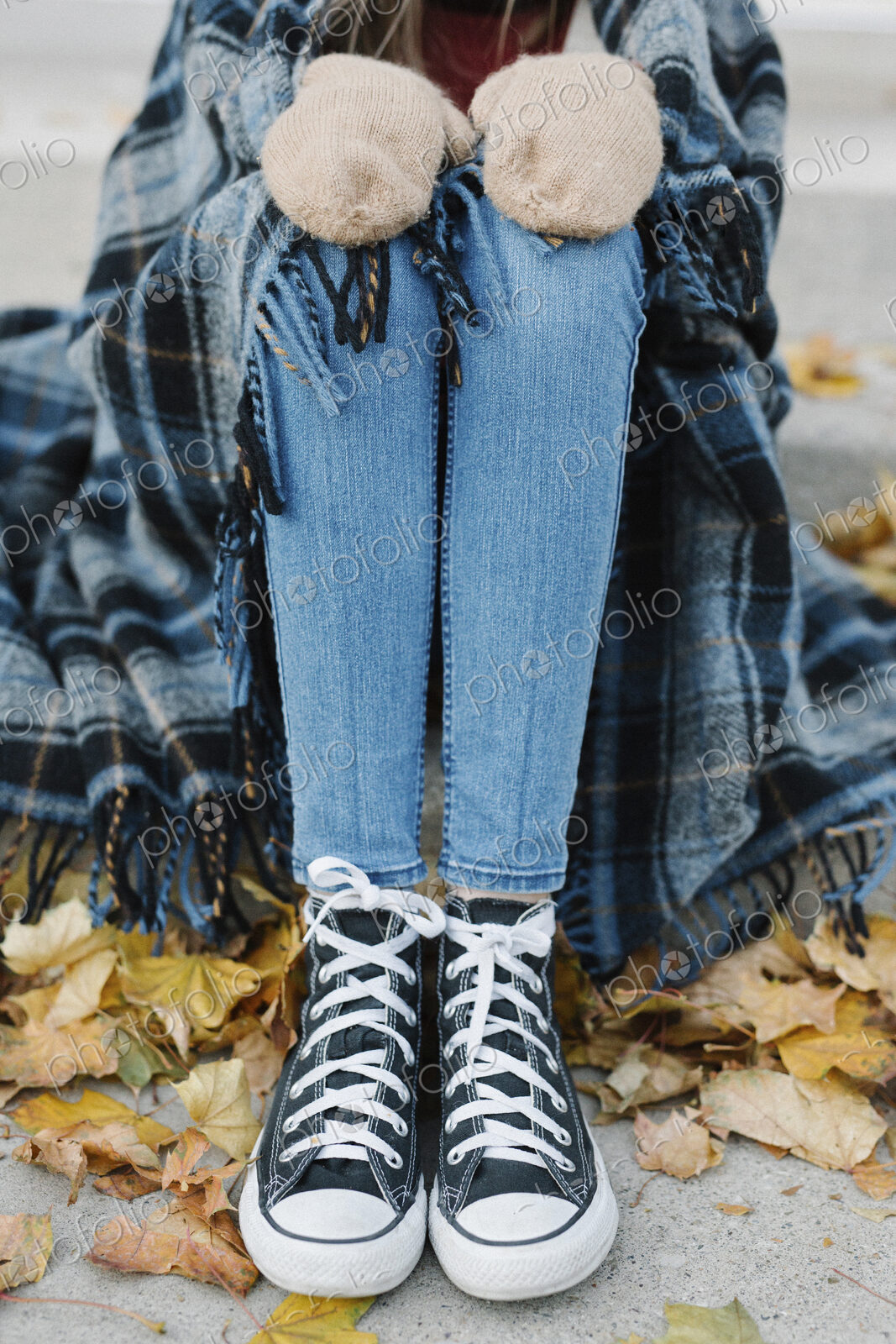 A young person sitting on a step with a warm plaid shawl around her.