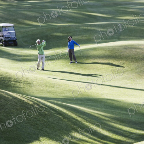 A young senior couple playing golf in the fairway of a golf course. A young senior couple playing golf in the fairway of a golf course.