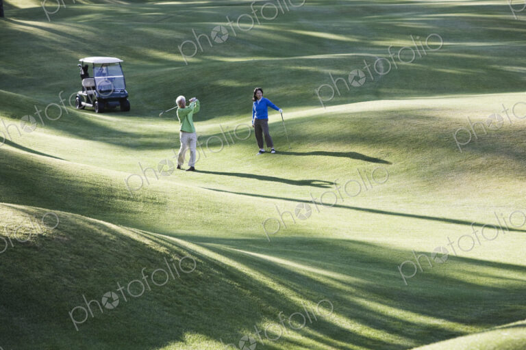 A young senior couple playing golf in the fairway of a golf course.