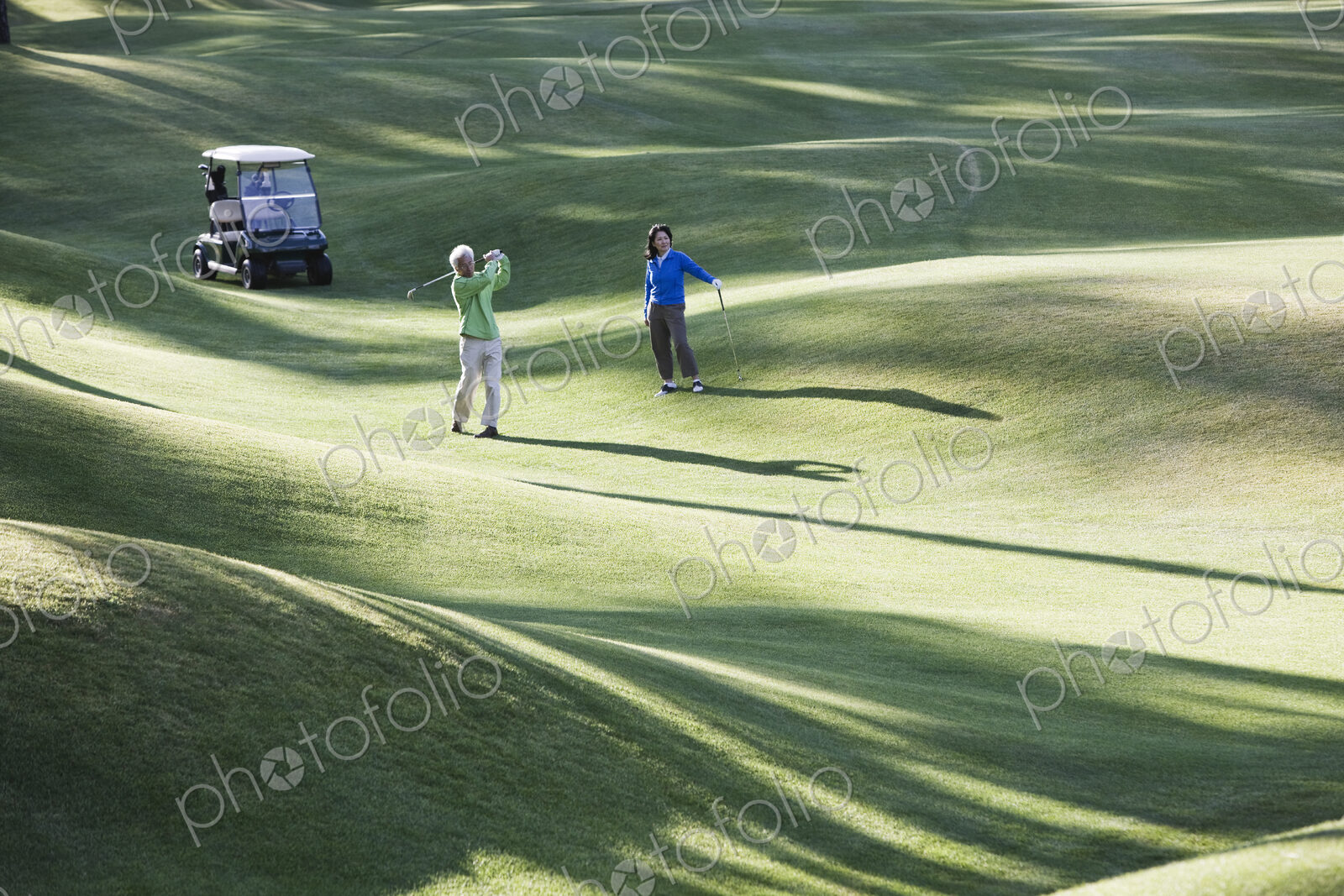 A young senior couple playing golf in the fairway of a golf course.