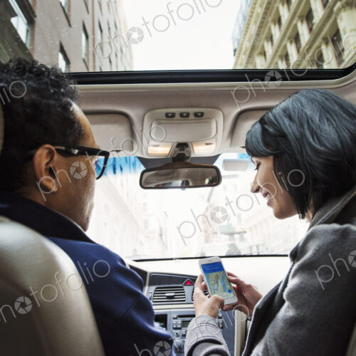 A young woman and young man in a car looking at a map on the display of a cellphone,… A young woman and young man in a car looking at a map on the display of a cellphone,…
