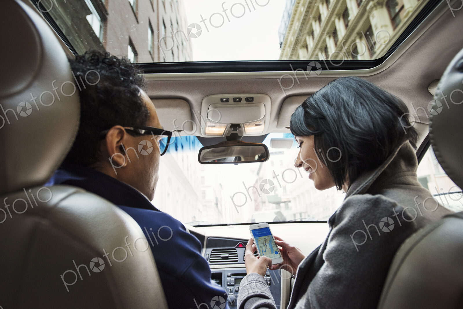 A young woman and young man in a car looking at a map on the display of a cellphone,…