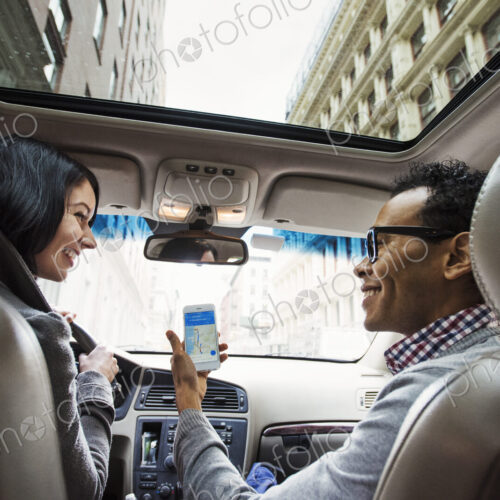 A young woman and young man in a car looking at a map on the display of a cellphone,… A young woman and young man in a car looking at a map on the display of a cellphone,…
