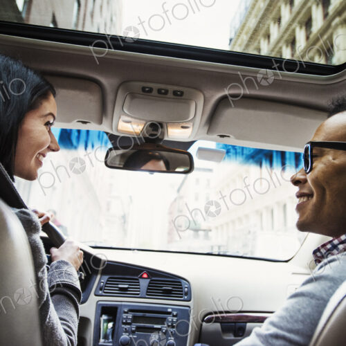 A young woman and young man in a car looking at each other and smiling, seen from the… A young woman and young man in a car looking at each other and smiling, seen from the…