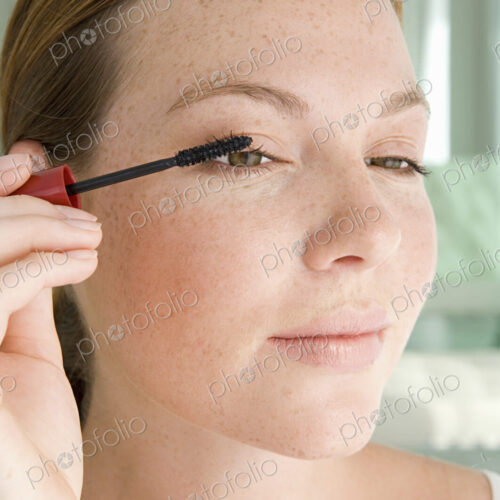 A young woman applying mascara to her eyelashes. A young woman applying mascara to her eyelashes.