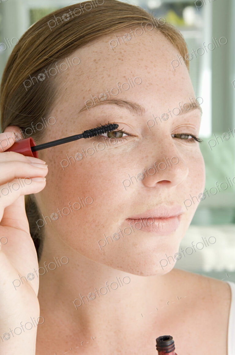 A young woman applying mascara to her eyelashes.
