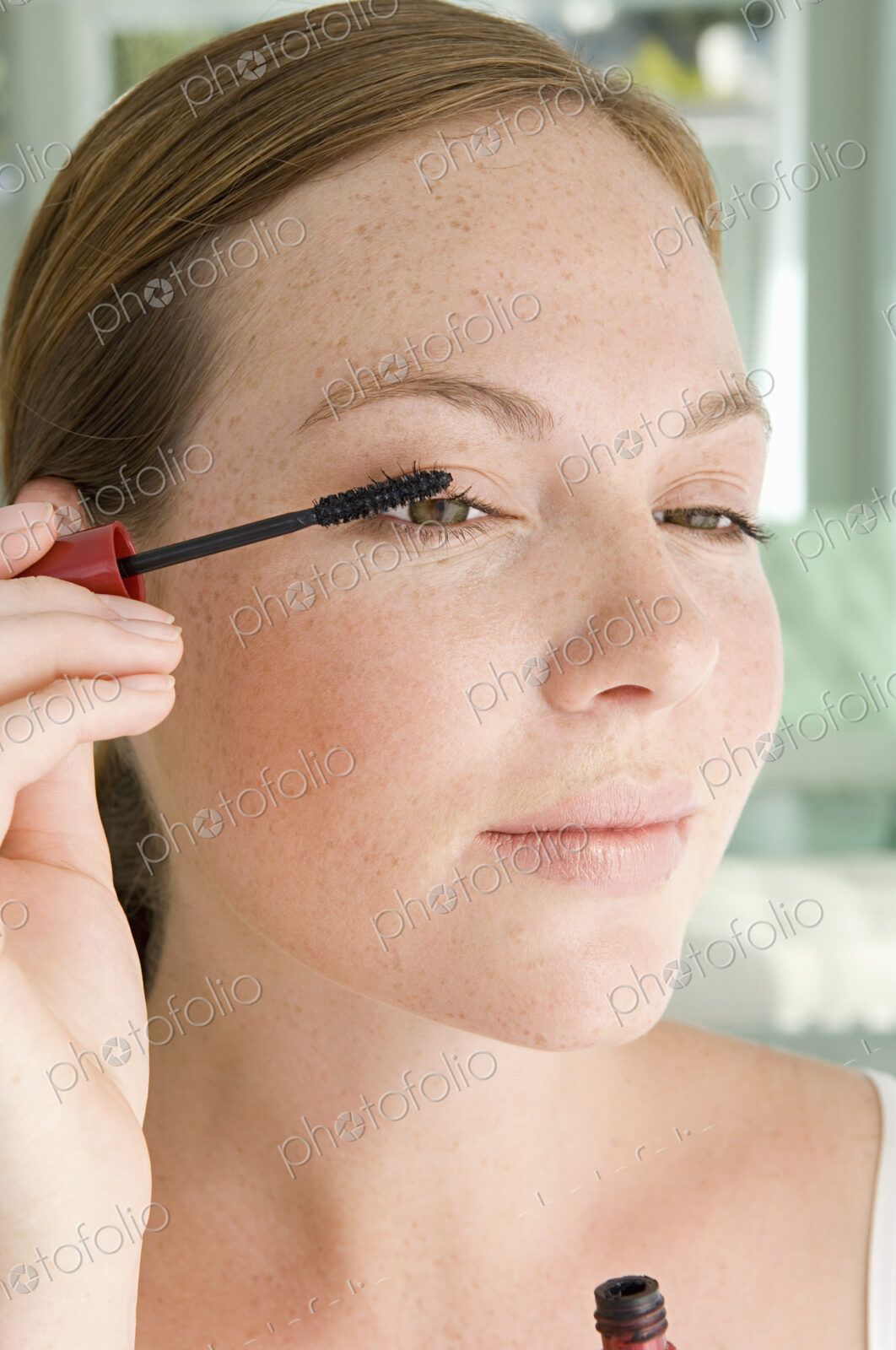 A young woman applying mascara to her eyelashes.