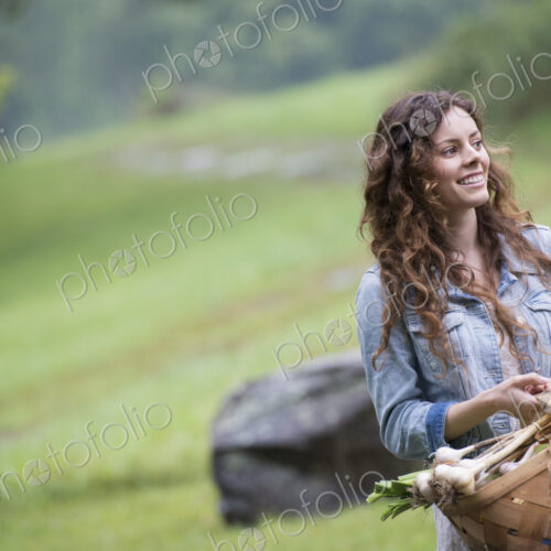 A young woman carrying a basket of freshly harvested garlic and vegetables.