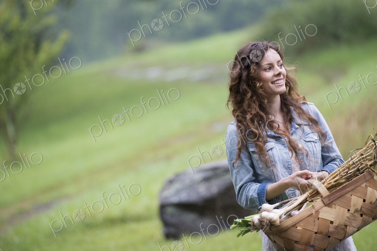 A young woman carrying a basket of freshly harvested garlic and vegetables.