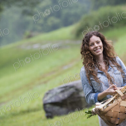 A young woman carrying a basket of freshly harvested garlic and vegetables.