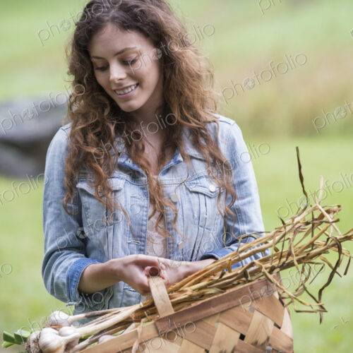 A young woman carrying a basket of freshly harvested garlic and vegetables.
