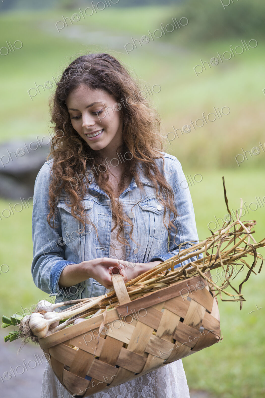 A young woman carrying a basket of freshly harvested garlic and vegetables.