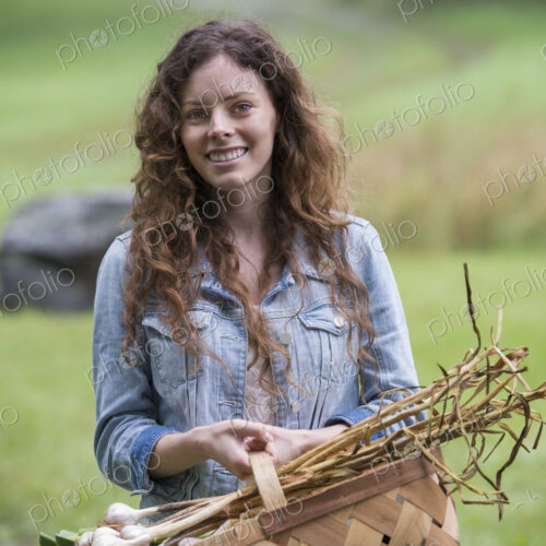 A young woman carrying a basket of freshly harvested garlic and vegetables.