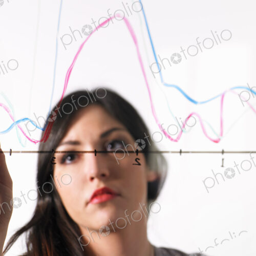 A young woman drawing coloured graph lines across a graph illustration, on a see… A young woman drawing coloured graph lines across a graph illustration, on a see…