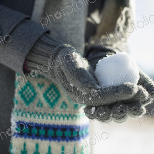 A young woman holding a small snowball in her gloved hands. A young woman holding a small snowball in her gloved hands.
