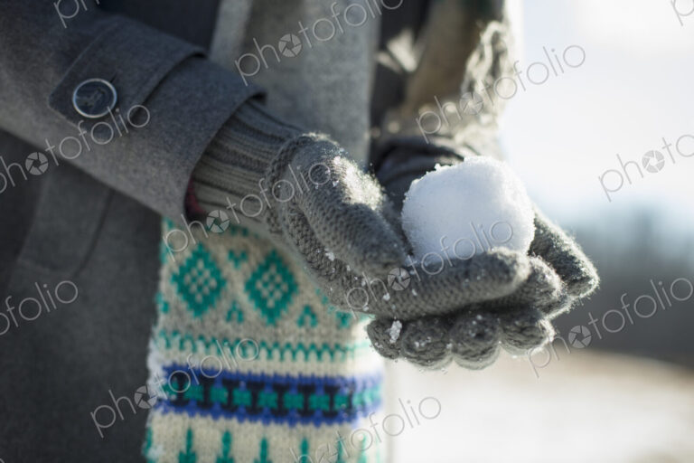 A young woman holding a small snowball in her gloved hands.