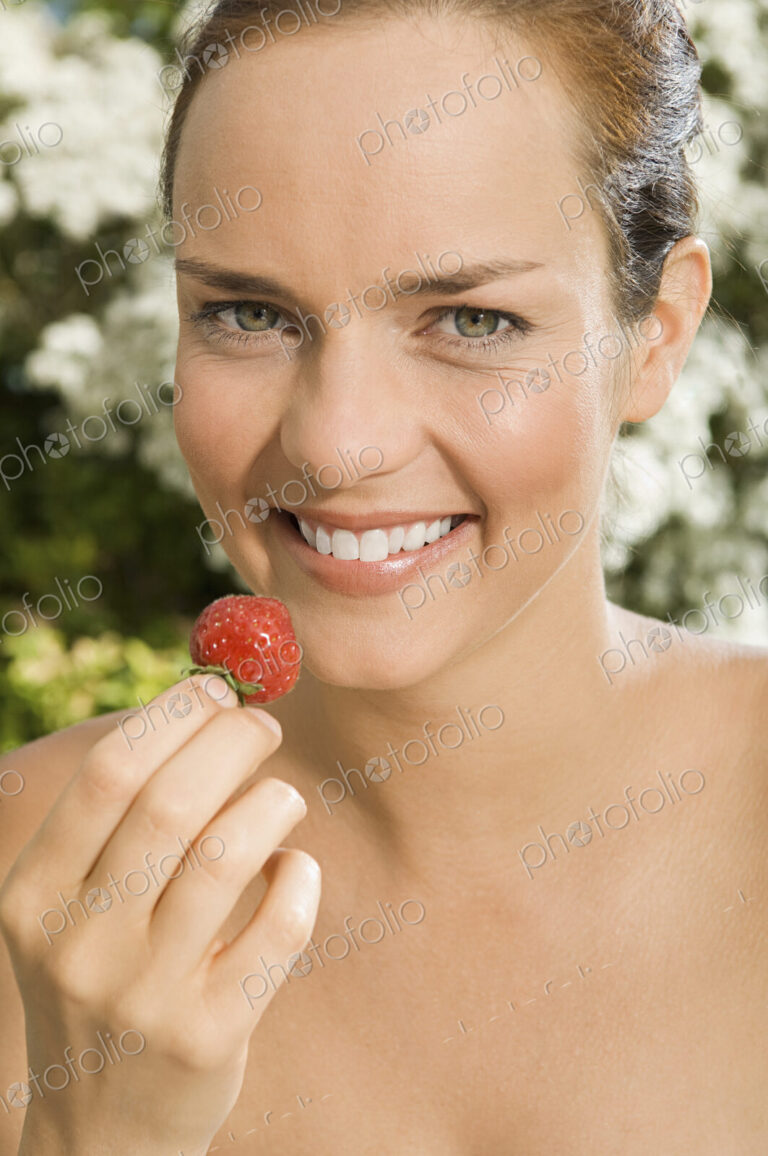 A young woman holding a strawberry.