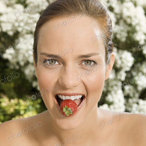 A young woman holding a strawberry between her teeth. A young woman holding a strawberry between her teeth.