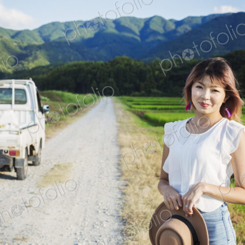 A young woman holding a sun hat, standing on a road by open fields of rice paddies. A young woman holding a sun hat, standing on a road by open fields of rice paddies.