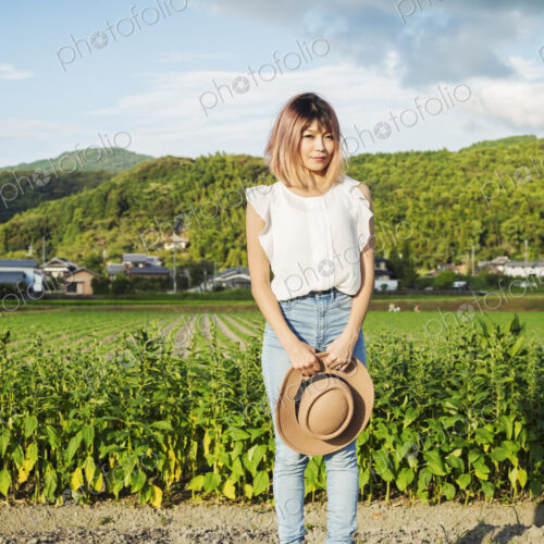 A young woman holding a sun hat, standing on a road by open fields of rice paddies. A young woman holding a sun hat, standing on a road by open fields of rice paddies.