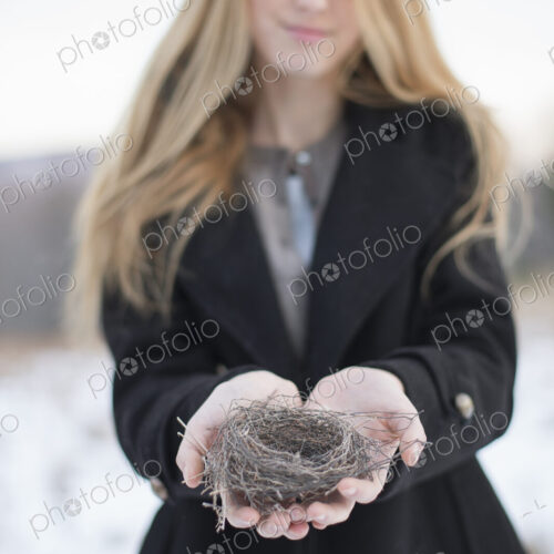 A young woman holding an old bird's nest in her hands, tightly woven twigs. Winter scene. A young woman holding an old bird's nest in her hands, tightly woven twigs. Winter scene.