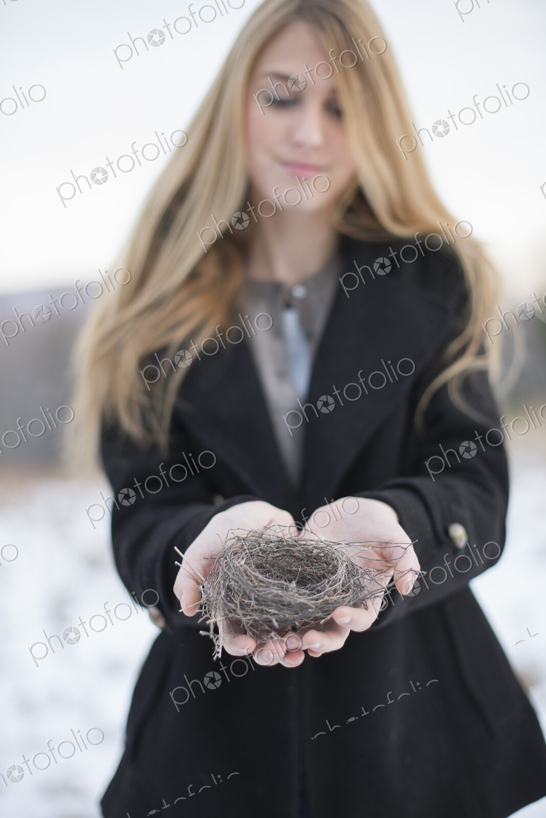 A young woman holding an old bird’s nest in her hands, tightly woven twigs. Winter scene.