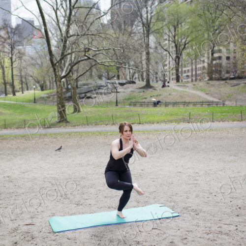 A young woman in Central Park, in a black leotard and leggings, doing yoga.
