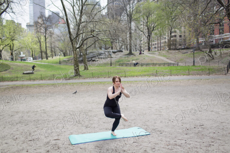 A young woman in Central Park, in a black leotard and leggings, doing yoga.