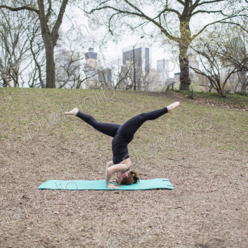 A young woman in Central Park, in a black leotard and leggings, doing yoga.