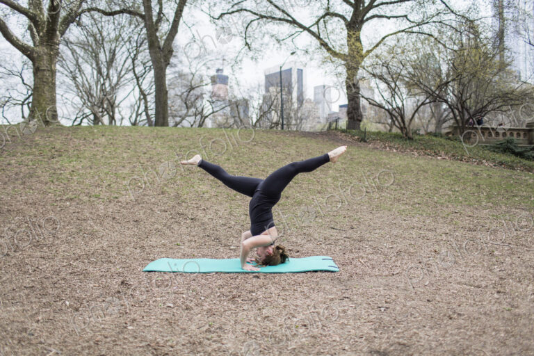 A young woman in Central Park, in a black leotard and leggings, doing yoga.